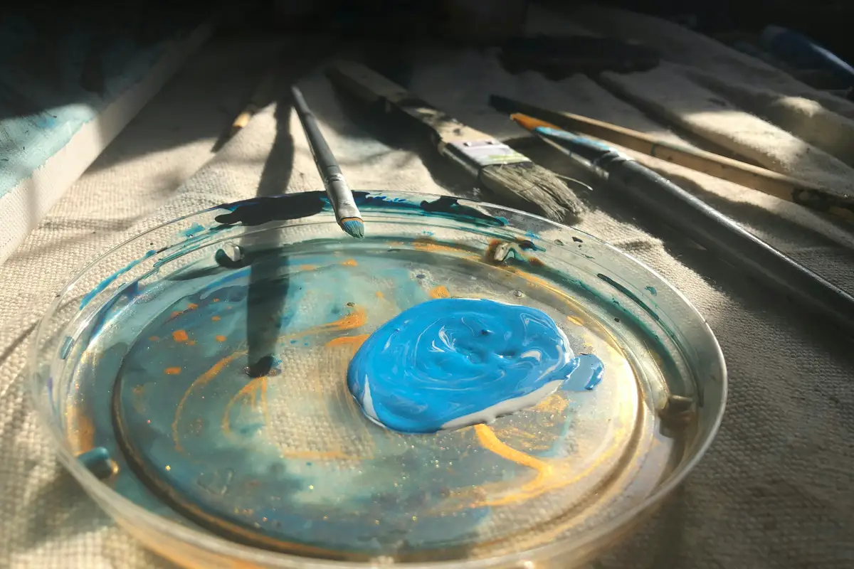 Paleta redonda con una mancha de pintura azul claro y varios pinceles al lado, mezcla base del turquesa – totenart