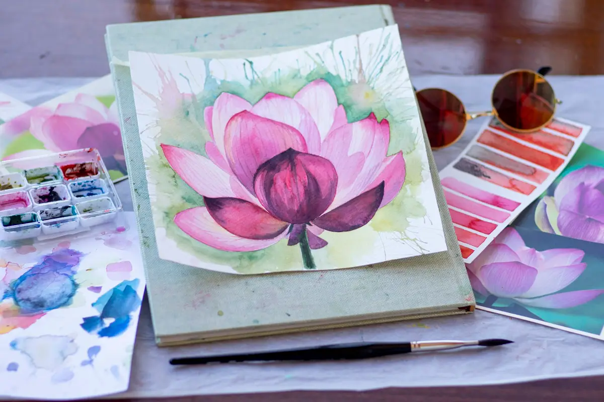 Acuarelas fáciles: 10 ideas para empezar a pintar 5 Acuarela de una flor de loto rosa sobre un cuaderno, junto a una paleta y muestras de color – Totenart