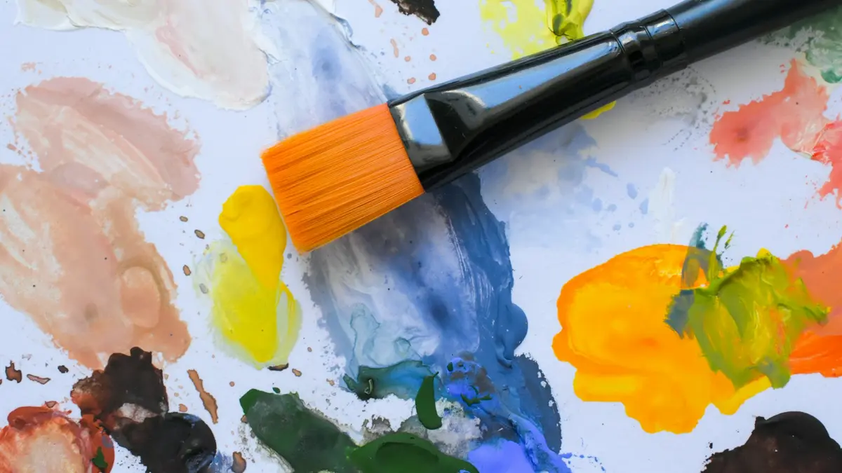 Pincel con pintura naranja sobre una paleta con manchas de amarillo, rojo y azul – Totenart